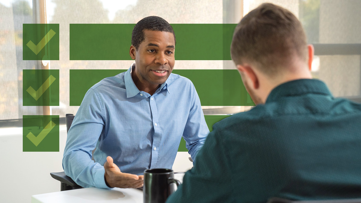 Two men sit at a table engaged in discussion, with one gesturing openly.