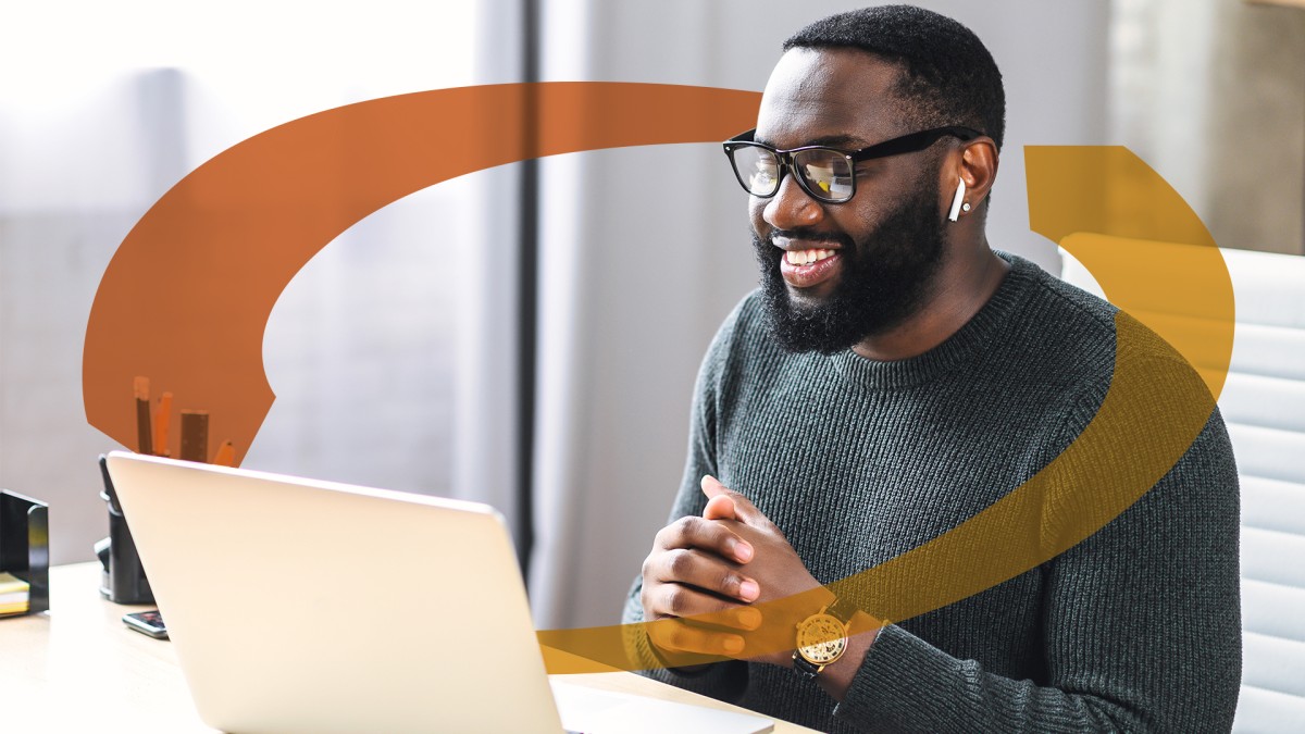 A man with glasses and earbuds smiles while on a video call at his laptop.