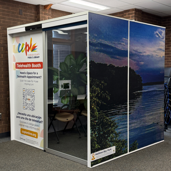  A telehealth booth in a library, featuring a serene bay scene on its exterior. The booth provides privacy with a seated area inside. 