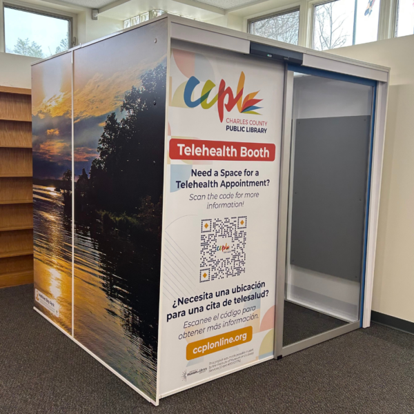 Telehealth booth in a library corner; features sunset nature mural and informational sign with contact details in English and Spanish, inviting appointments.